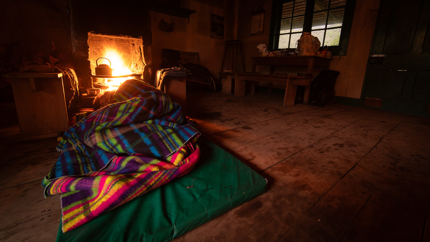 Dark room with colorful blanket on a bed and light source creating shadows