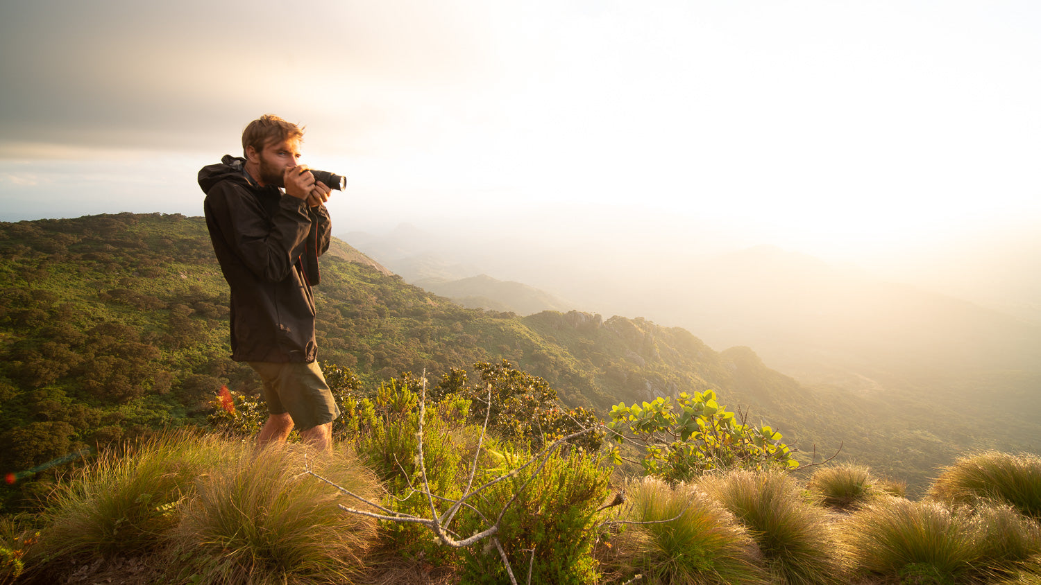 Man taking a photograph in a scenic outdoor setting with mountains and greenery.