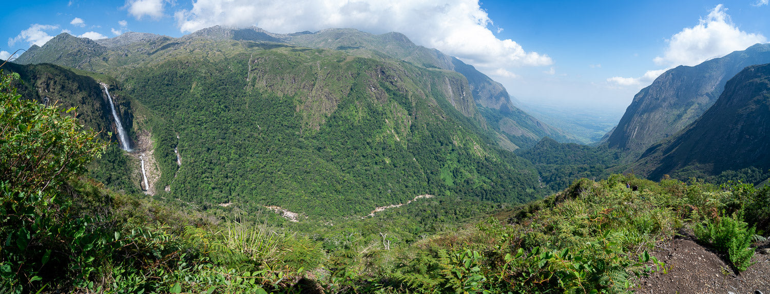 Scenic view of mountains and valleys with a waterfall, under a blue sky with clouds.